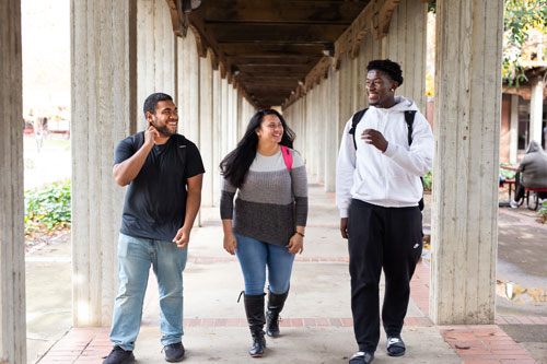 three students walking together on campus and smiling in conversation